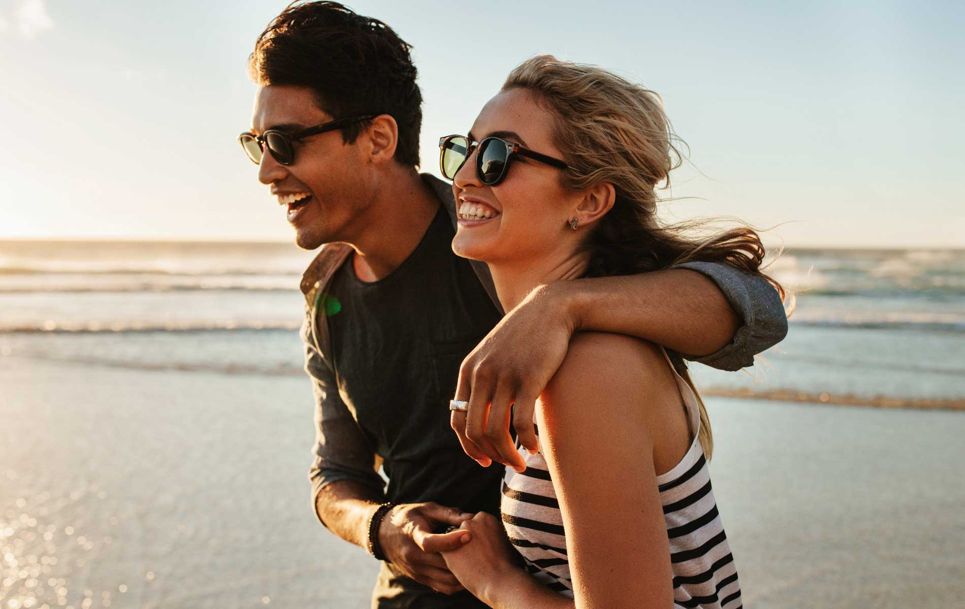 Couple walking on the beach wearing Polarised sun glasses