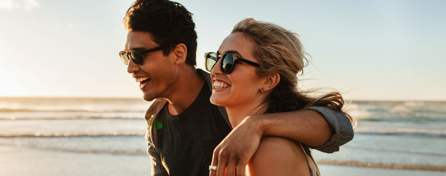 Couple walking on the beach wearing Polarised sun glasses