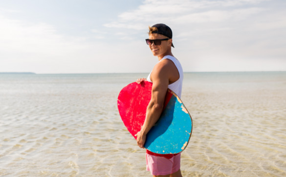 Man with surfboard on the beach wearing polarised sun glasses